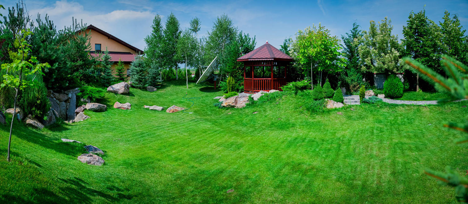 Peisaj verde și îngrijit cu gazon perfect, zonă de relaxare cu foișor și pietre decorative în grădina de acasă