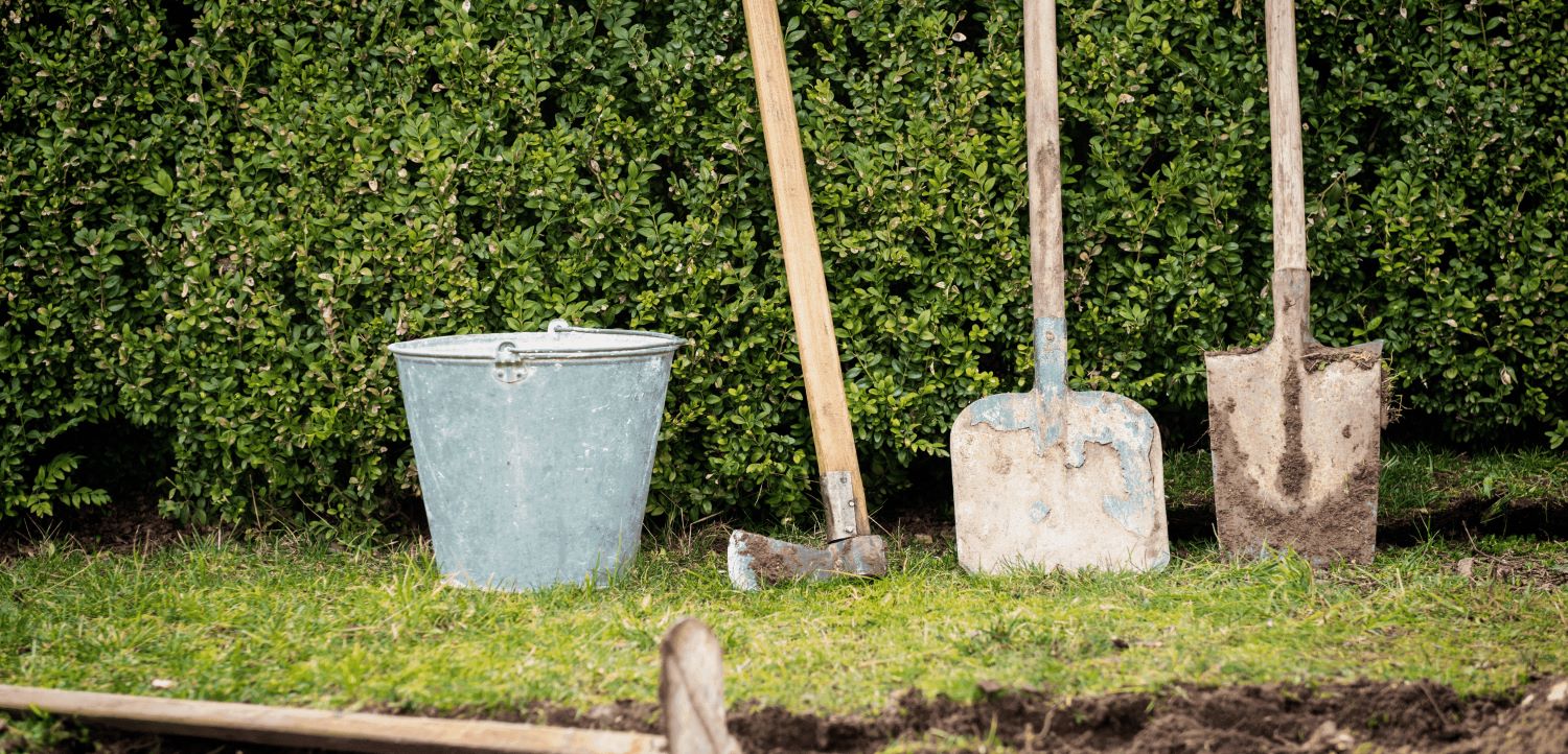 Unelte de grădinărit esențiale pentru întreținerea gazonului primăvara, inclusiv lopeți, topor și găleată.