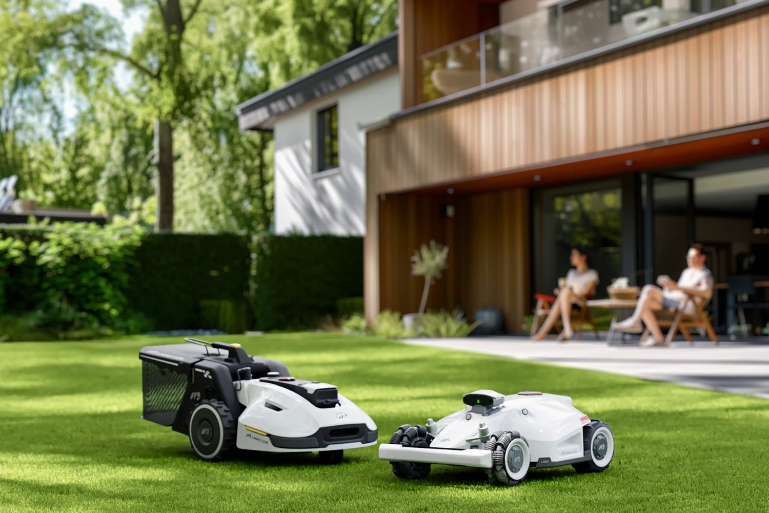 Robotii Mammotion Luba și Yuka pe un gazon verde, proaspăt tuns și o familie care se relaxează fără grija tunderii gazonului, pe fundal